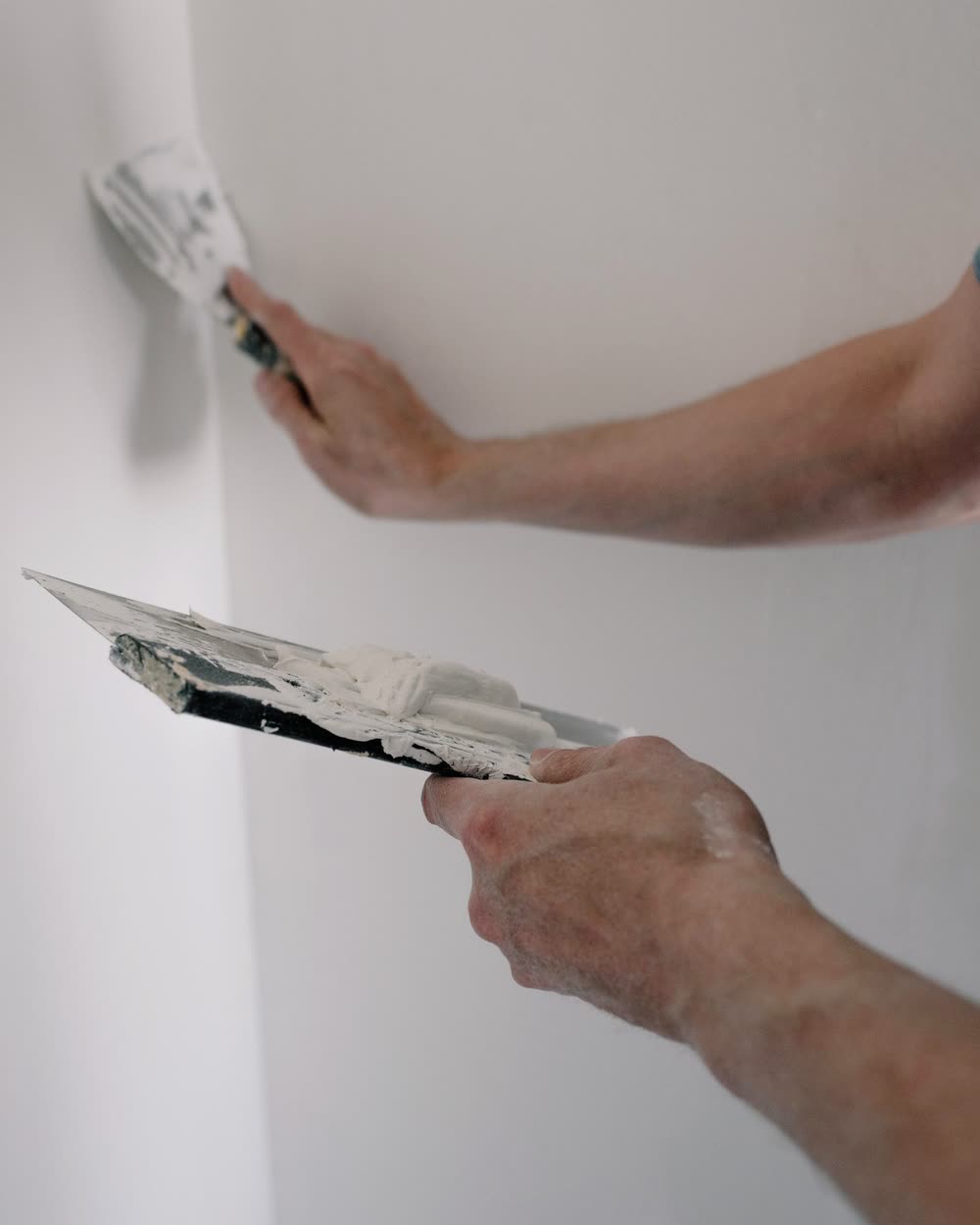 A plasterer smoothing a wall by hand with two steel finishing trowels